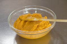 a small bowl filled with yellow food on top of a table next to a wooden spoon