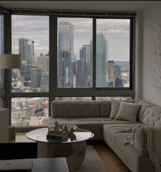 a living room filled with furniture and large windows overlooking the cityscape in the distance