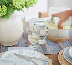 a person pours white wine into a glass on a table with plates and silverware