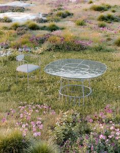 two tables and chairs sitting in the middle of a field with wildflowers around them