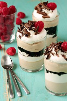 three desserts with raspberries and whipped cream in them on a blue table