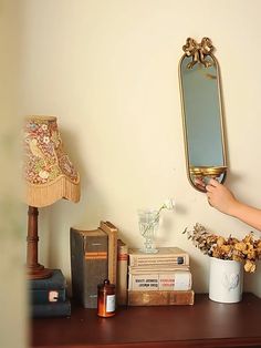 a person holding a mirror above a table with books and vases on top of it