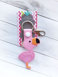 a pink flamingo key fobring on a white wooden surface with a tag attached to it