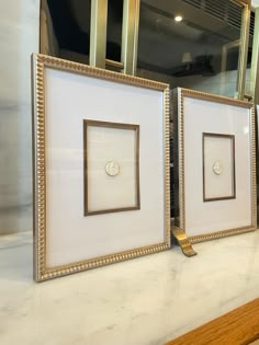 two framed pictures sitting on top of a counter in front of a mirror with gold trim