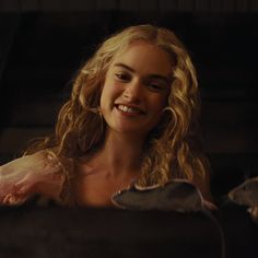 a woman with long blonde hair smiling and holding a piece of meat in her hand