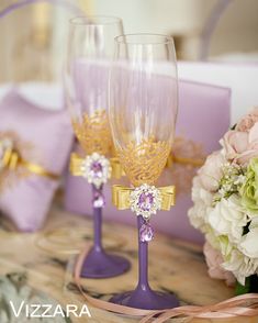 two wine glasses sitting on top of a table next to purple boxes and white flowers