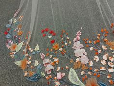 an embroidered fabric with flowers and leaves on the ground in front of a wall hanging