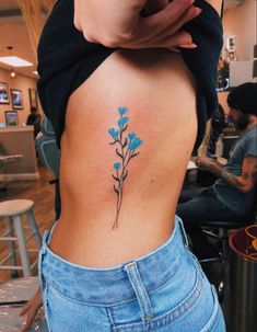 a woman's lower back tattoo with blue flowers on her left side ribcage