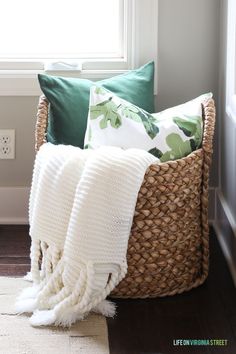 a basket filled with pillows and blankets next to a window