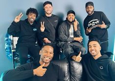 a group of men standing next to each other in front of a blue wall with their thumbs up