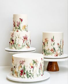 three tiered cakes decorated with flowers and leaves on white platters next to each other