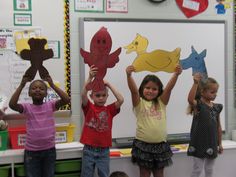 four children holding up paper animals in front of a whiteboard