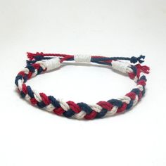 a red, white and blue rope bracelet on a white table with a black hook