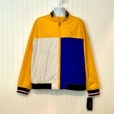 Classic Yellow & Blue Colorblock Lightweight Varsity Bomber Jacket From Tommy Hilfiger In Men's Size Xxl (2xl). Measurements: 56" Chest | 54" Waist | 48-56" (Stretchy) Hem/Hips | 29" Length | 28" Sleeves. Men's Jacket Is Colorblocked With Yellow, White And Blue Colors. Full Zip Front. Classic Bomber Jacket Style With Stretchy Banded Hem And Sleeve Cuffs. Hem Is Navy Rib Knit. Sleeves Are Striped Rib Knit. Long Sleeve Length. Logo On The Chest And On The Left Sleeve. Stand Collar -- Rib Knit On T Long Sleeve Yellow Color Block Outerwear, Winter Yellow Color Block Outerwear, Sporty Blue Tommy Hilfiger Outerwear, Yellow Color Block Outerwear For Spring, Spring Yellow Color Block Outerwear, Vintage Tommy Hilfiger Jackets, Military Style Jackets, Tommy Hilfiger Jackets, Blue Jean Jacket