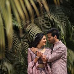 a man and woman standing next to each other in front of some palm tree leaves