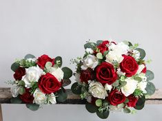 two red and white bouquets sitting on top of a wooden table next to each other