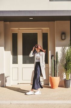 a woman standing in front of a house next to a cactus and potted plant