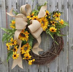 a wreath with sunflowers and greenery tied to it on a wooden fence