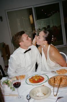 a man and woman sitting at a table with food in front of them, kissing