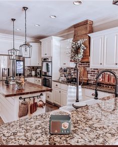 a kitchen with white cabinets and granite counter tops, an island in the middle is surrounded by hanging lights