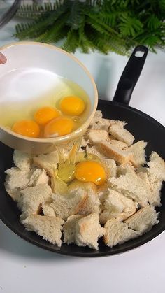 someone is pouring eggs into some bread on a black plate with green plants in the background