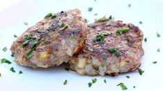 two meat patties on a white plate with parsley sprinkled on top