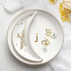 three pieces of jewelry on a plate next to yellow flowers and a white table cloth