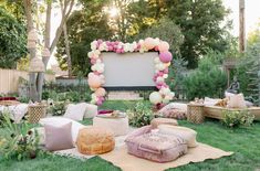 an outdoor movie screen surrounded by pillows, blankets and other decorations on the grass with trees in the background