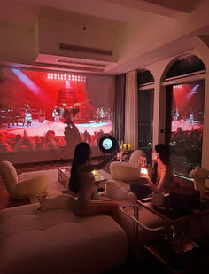 two women sitting on couches in front of large windows with red lights shining through them