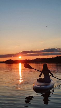 a person on a paddle board paddling in the water at sunset with the sun setting