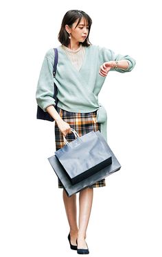 a woman in a green sweater and plaid skirt holding a black bag with her right hand