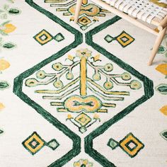 a white rug with green and yellow designs on the floor next to a wooden chair