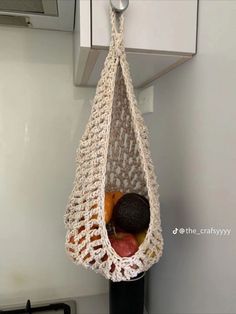 a crocheted bag hanging from the side of a stove with fruit in it