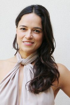 a woman with long dark hair wearing a beige top and smiling at the camera,