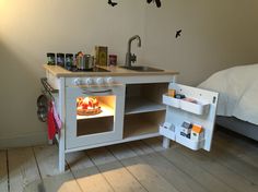 a small white stove top oven sitting inside of a kitchen next to a bed and sink