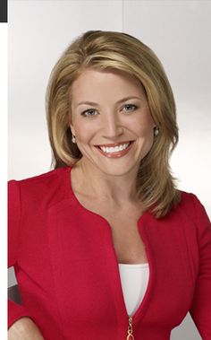 a woman wearing a red jacket and white shirt smiling at the camera with her hands on her hips