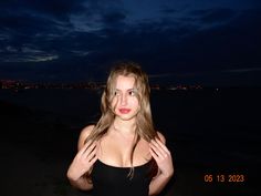 a woman standing on the beach at night with her hands in front of her face