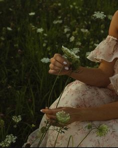 a woman is sitting in the grass with some wildflowers on her hand and she is wearing a pink dress