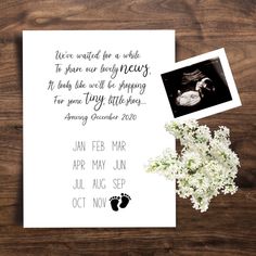 a baby announcement is shown on top of a wooden table next to a bouquet of flowers