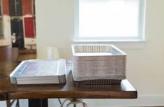 a wooden table topped with books and a metal basket on top of it next to a window