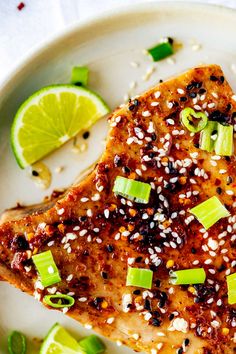 a white plate topped with meat covered in sesame seeds and green onions next to sliced limes