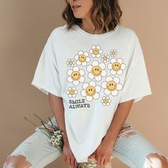 a woman in white t - shirt with smiley faces on it and flowers behind her