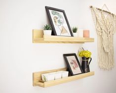 two wooden shelves with pictures and other items on them in a white walled room next to a macrami wall hanging