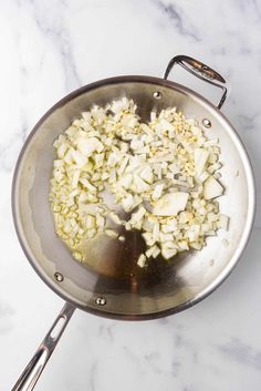 onions being cooked in a pan on a marble counter top with tongs and seasonings