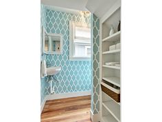 a bathroom with blue and white wallpaper and shelving unit in the corner, along with wooden flooring