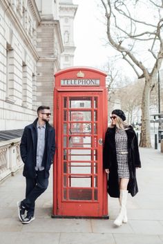 a man and woman standing next to a red phone booth