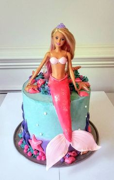 a barbie doll sitting on top of a blue and green cake with pink frosting