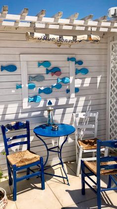 two chairs and a table with fish on the wall behind them in front of a white house