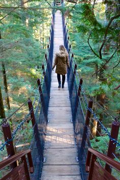 a woman walking across a suspension bridge in the woods