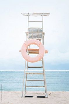 lifeguard chair on the beach with an inflatable life preserver by luma photography for stocksy magazine